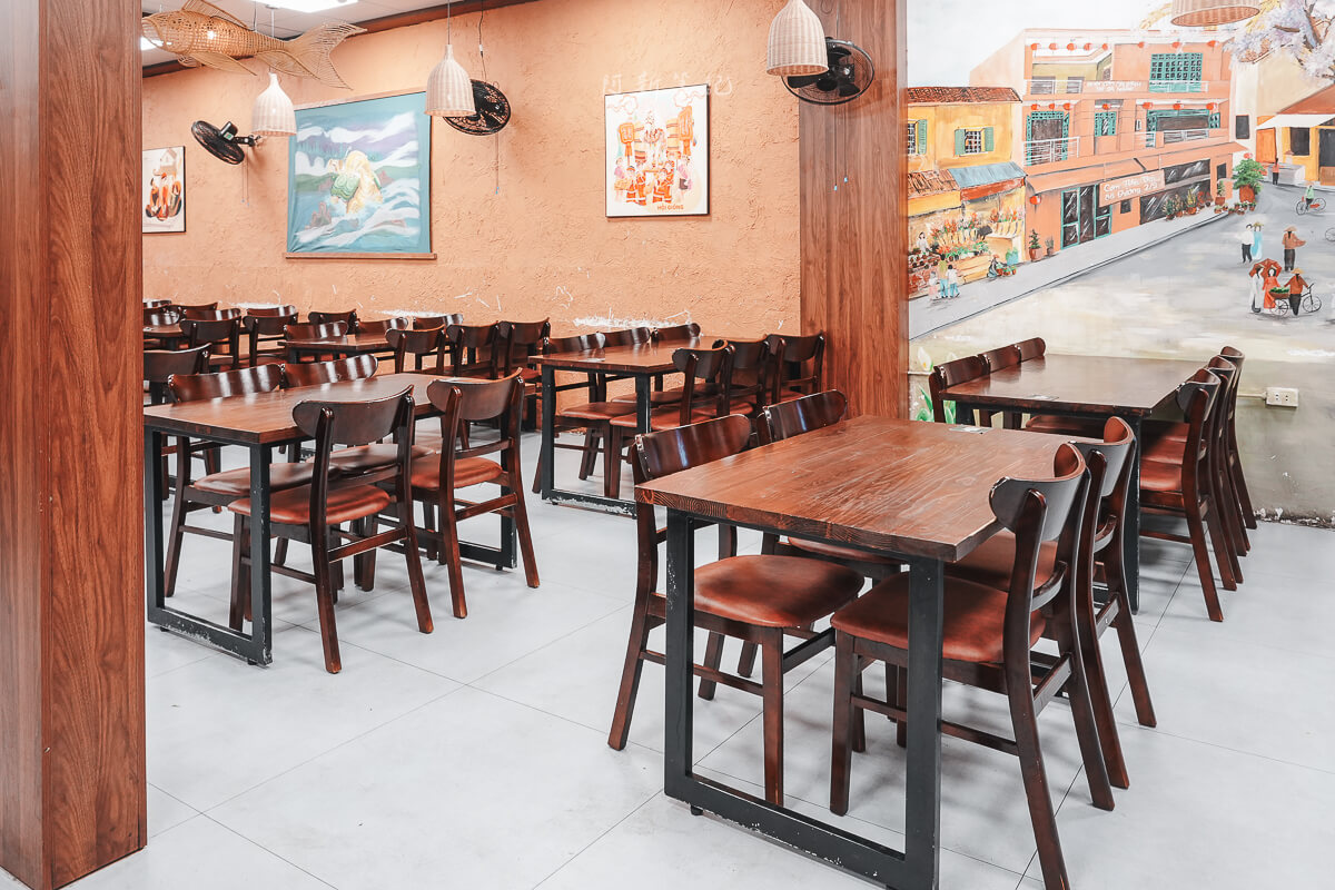 峴港 Com Nha Vui 室內用餐區的木桌、椅子與牆面裝飾