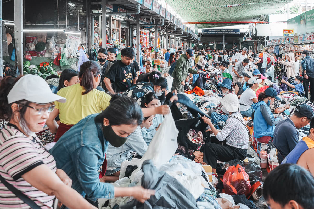 峴港共市場小吃攤旁，客人坐在矮凳上用餐，桌上是碗與調味料