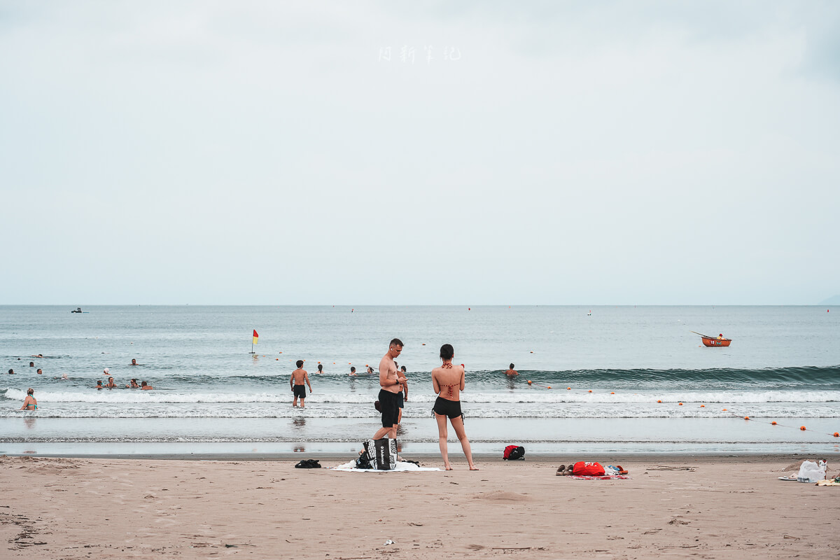 峴港海灘淺水區有遊客散步與玩水，遠方可見海平線