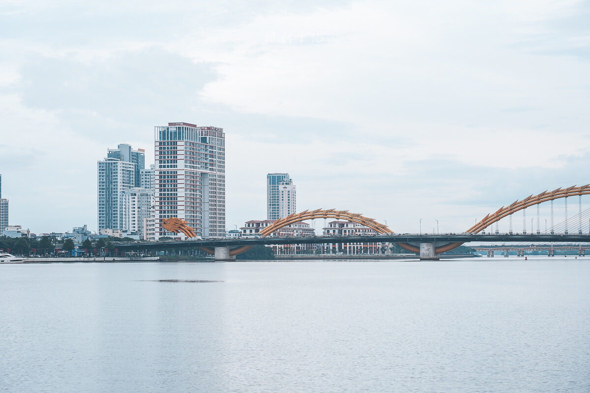 從峴港河岸看龍橋的龍頭與黃色橋身，後方是陳氏李橋