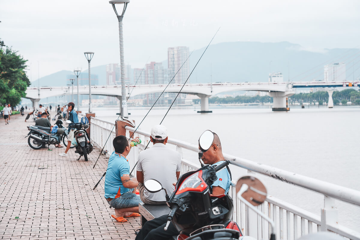 峴港韓江河岸欄杆邊釣魚的當地人，背景是韓江橋