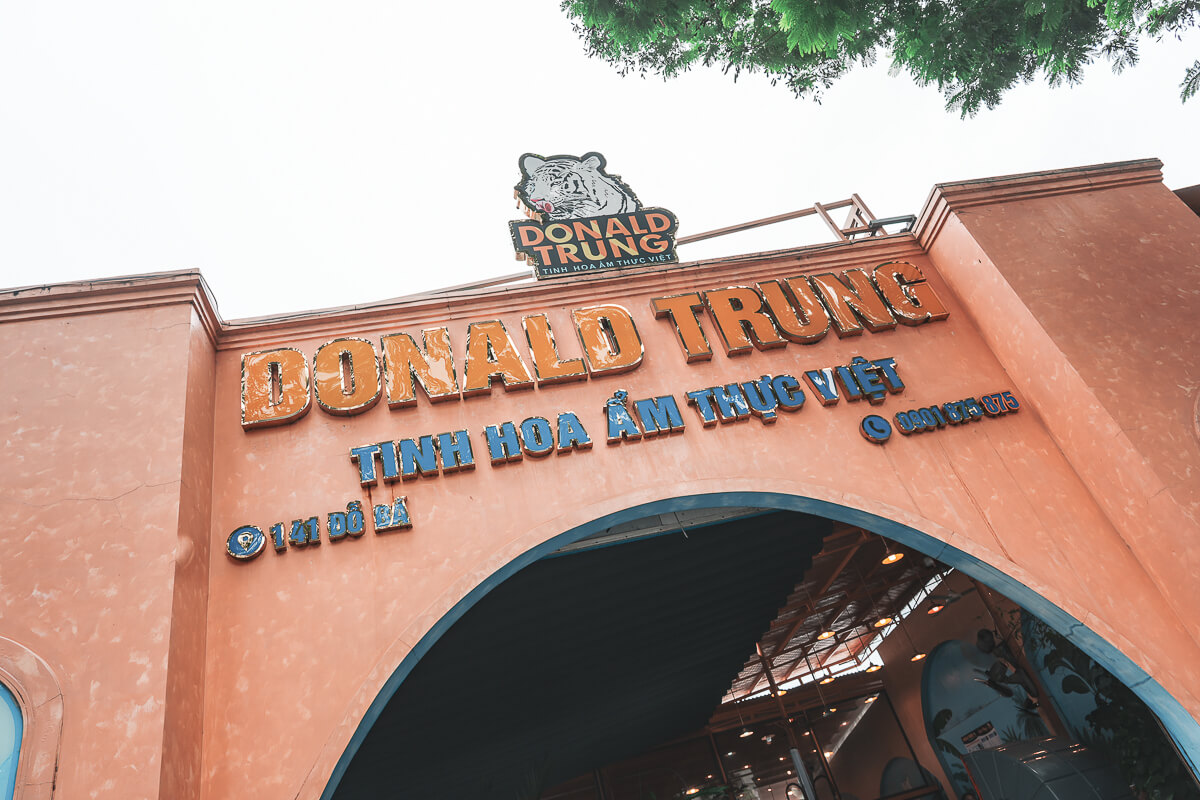 峴港 Donald Trung 招牌,峴港必吃餐廳 仰拍峴港 Donald Trung 橘色拱門上的店名招牌、老虎 logo 與地址電話