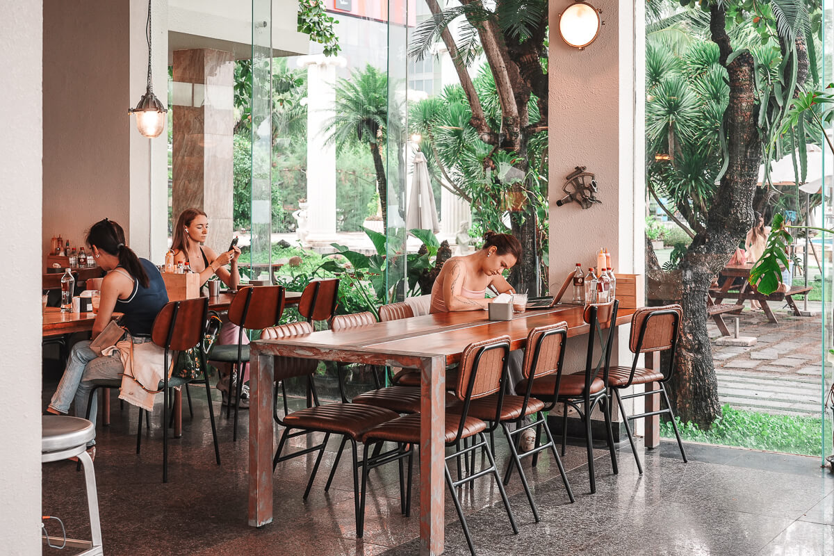 峴港 Lighthouse Coffee 明亮的用餐區，木桌椅周圍搭配綠色植栽