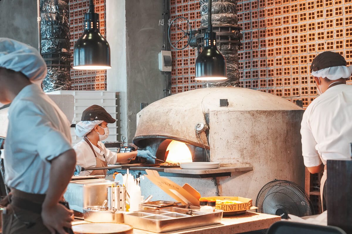 峴港 Pizza 4P's Indochina 開放式廚房，廚師在柴燒窯爐前製作披薩