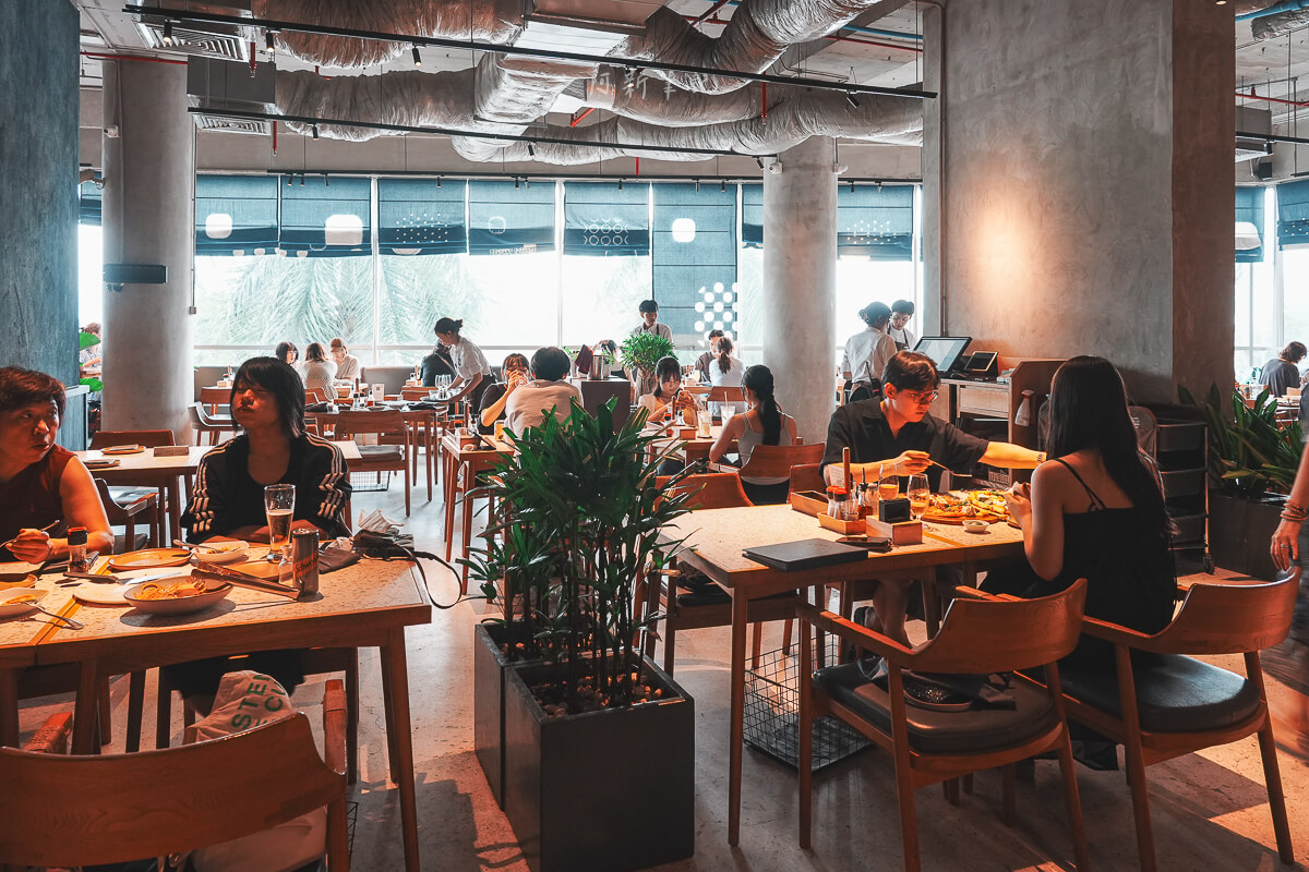 峴港 Pizza 4P's Indochina 店內木桌椅、水泥柱、藍色窗簾與用餐人潮