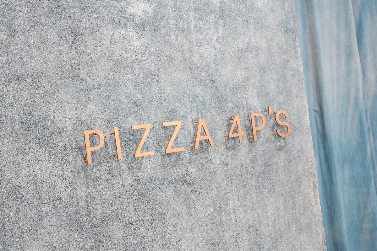 峴港 Pizza 4P's Indochina 灰藍色水泥牆上的銅色 PIZZA 4P'S 店名標誌