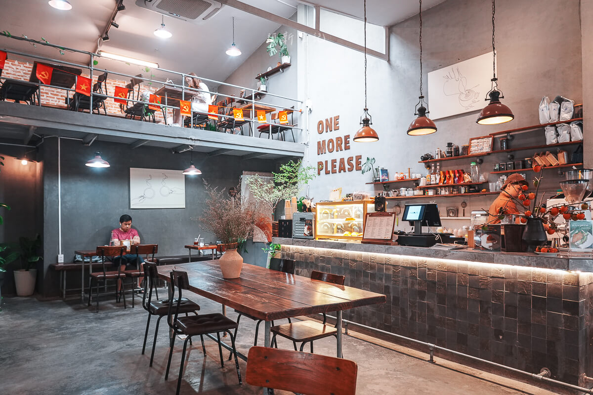 峴港 The Hideout Cafe 室內全景，灰磚吧檯、長木桌、ONE MORE PLEASE 木字與二樓欄杆