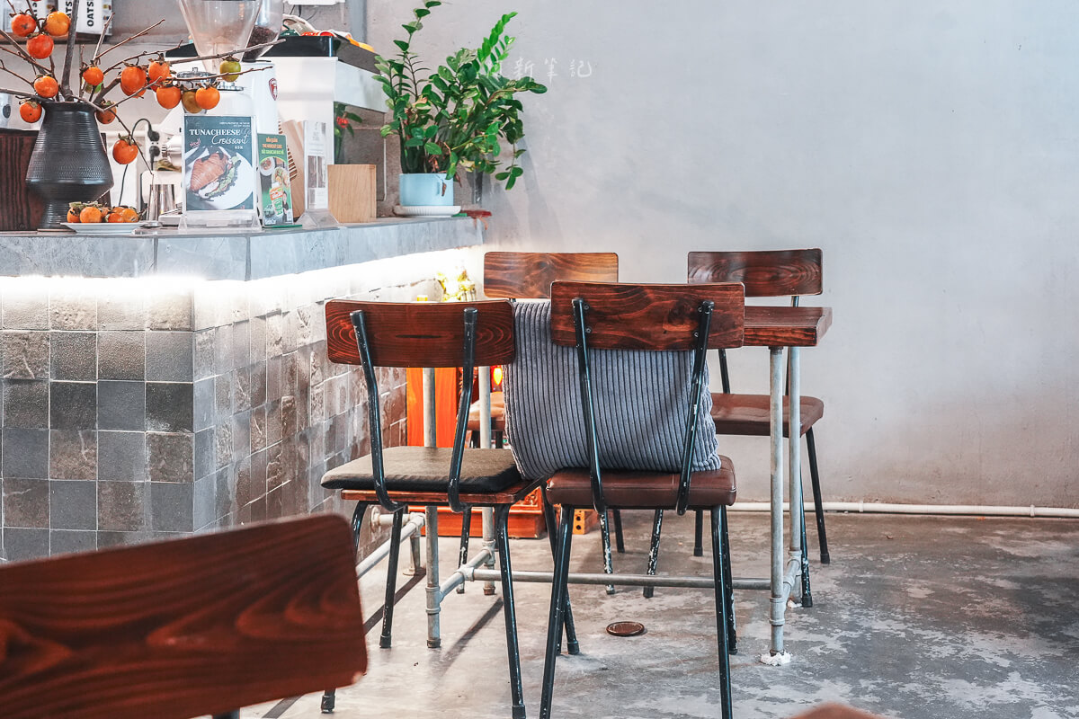 峴港 The Hideout Cafe 靠吧檯的皮墊黑鐵椅與原木椅背，後方是灰磚吧檯與鮪魚起司可頌立牌